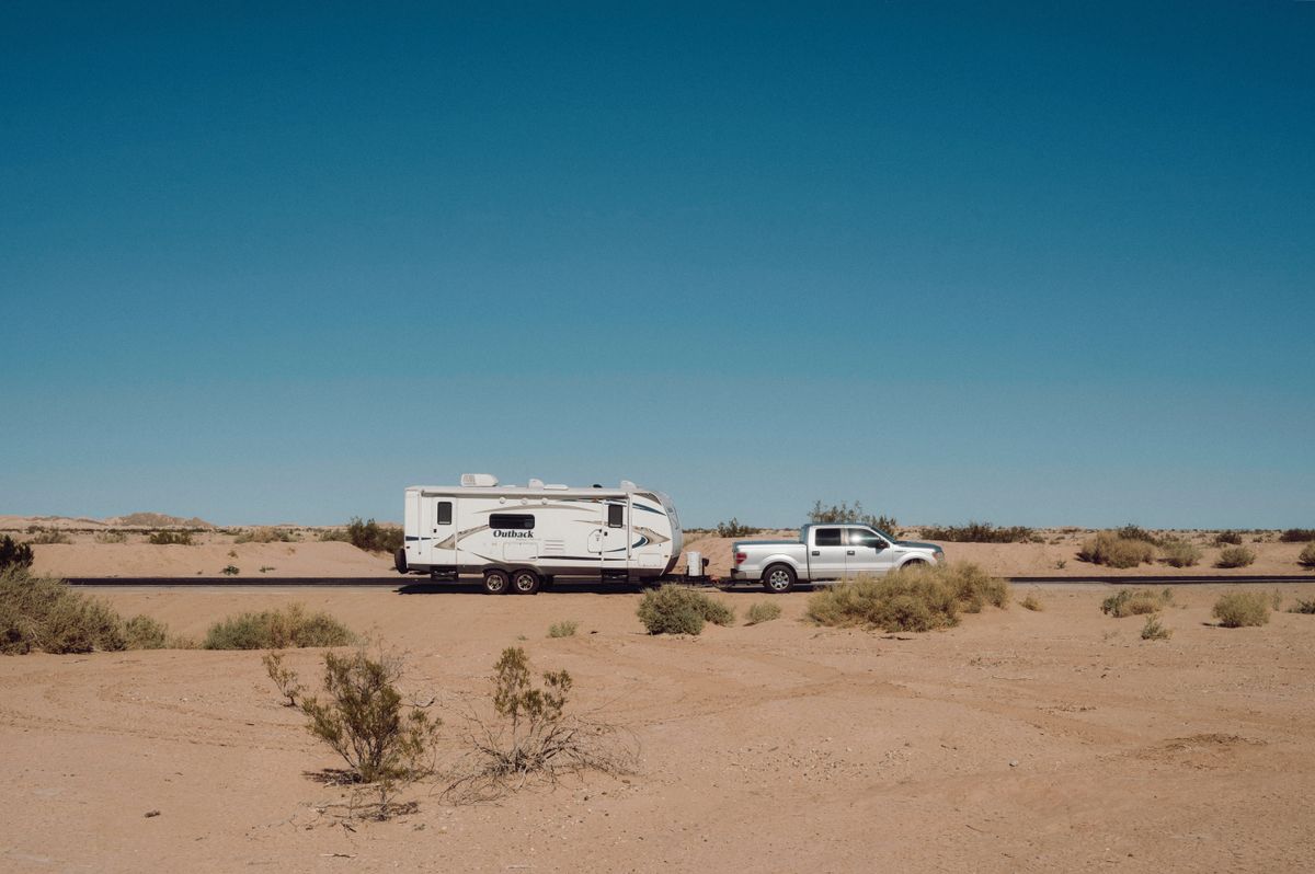 Pickup truck towing a travel trailer across open desert under a clear blue sky